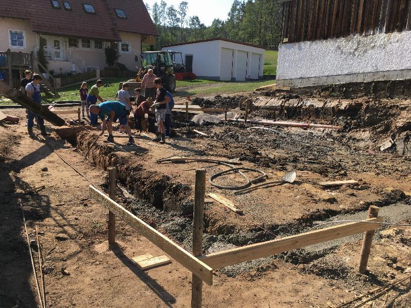 Nachdem Christian Riß das Grundstück im Ortskern zur Verfügung gestellt und das Büro Franz Lang die Planung für das Gemeinschaftshaus entworfen hatte, wurde im September 2018 die Baumaßnahmen mit dem Erdaushub, dem Einbringen einer Bodenplatte und dem Errichten einer Stützmauer begonnen. Dabei packten Jung wie Alt an. - Foto von Werner Schulz