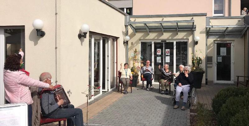 Dank Erwin Meier (vorne 2.v.l.) gab es für die Evergreen-Senior*innen willkommene Abwechslung von der seit Wochen herrschenden Corona-Monotonie. Spontan entsprach der Bitte von Sifa Heldmann (l.), der Chefin des Betreuungsteams, und erfreute die Heimbewohner*innen mit bekannten Liedern, in die sie gerne und lautstark einstimmten.

 - Foto von Werner Schulz