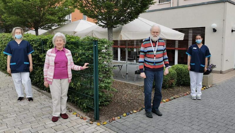 Auf Initiative der Evergreen-Sozialdienst-Mitarbeiterin Veronika Kizilok (r.) werden die Gehsteigränder um das Seniorenzentrum Evergreen mit selbstbemalten bunten Steinen dekoriert. Unterstützt wurde sie von ihrer Kollegin Olga Panin (l.), dem Sozialdienst-Team, der Heimbewohnerin Ruth Paa (2.v.l.) und vom Heimbeirat Andreas Stauber (2.v.r.).  - Foto von Werner Schulz