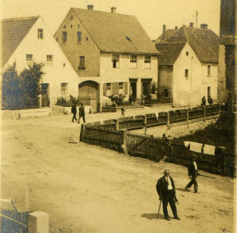 Schräg gegenüber dem Anwesen Pfab (1. Gebäude links) stand das Kassenhäuschen des Pflasterzolleintreibers Luber, bei dem der Knecht des Bauern Pongratz aus Steinginglohe zahlte, während sein Pferd alleine weiter ging. Nach gut 100 Metern kam es in der Nürnberger Straße zu dem für Georg Schiffer (mit Spazierstock) tödlichen, von dem scheuenden Pferd verursachten Verkehrsunfall. Zur Orientierung: Mittleres Gebäude = Kaufhaus Geiß/heute Physiotherapie Stenger, rechts daneben: Frisörladen Staudigl und Bäckerei Schneider/heute Heuberger. - Foto von Repros: Werner Schulz