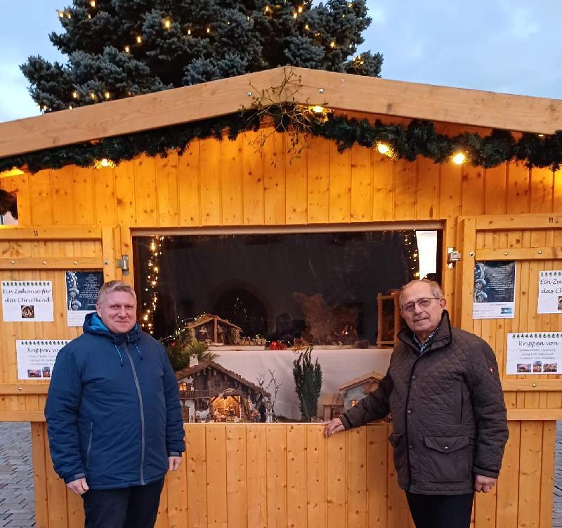 Neben dem Christbaum auf dem Marktplatz ist in einem Marktstand bis zum 6. Januar 2025 eine von Stadtrat Martin Merkl (links) organisierte Krippenausstellung zu besichtigen. Reinhold Birner (rechts) sperrt die Läden der Ausstellungsbude täglich um 8 Uhr auf und um 20 Uhr zu. - Foto von Werner Schulz