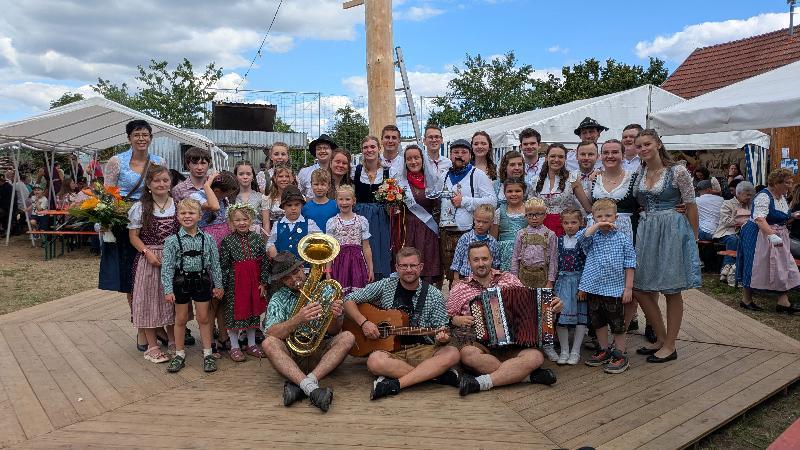 Bei der 14. Steiningloher Stodlkirwa tanzten 18 Kinder und sieben Kirwapaare um den 30 Meter hohen Kirwabaum. Als Oberkirwapaar wurden Sophia Pfab und Jonas Weiß (Bildmitte mit Blumenstrauß bzw. Kirwaliesl) ermittelt. Links hinten: Tanzlehrerin Eva Pfab, die seit zehn Jahren die Tänze einstudiert. Vorne das Trio „D’Allerscheynst’n“, das beim Austanzen aufgespielt hat. - Foto von Werner Schulz